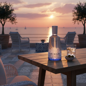 Botella de Gin Mare sobre una mesa, con un aperitivo servido, disfrutando de un atardecer frente al mar.